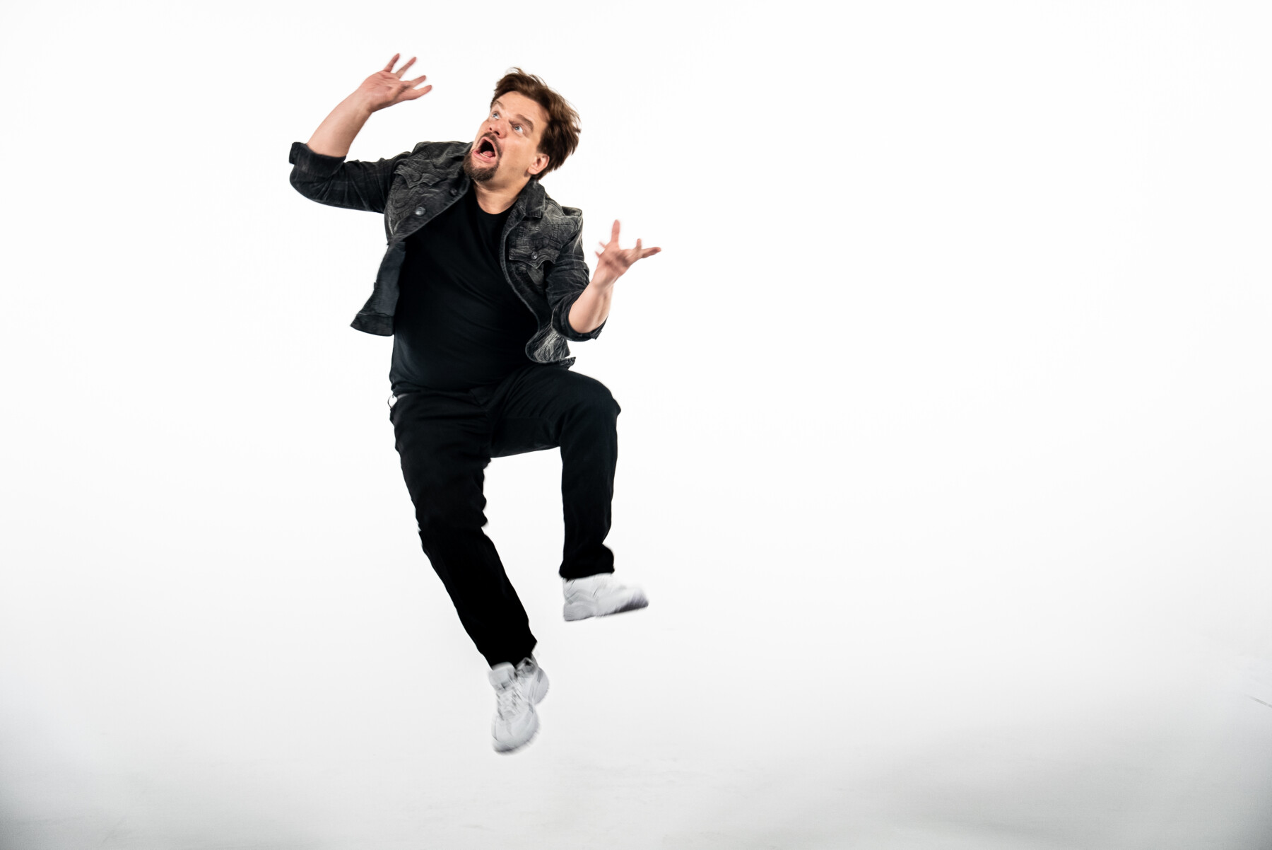 Ismo Leikola jumps into the air against a plain white background, throwing his hands up with an exaggerated expression.
