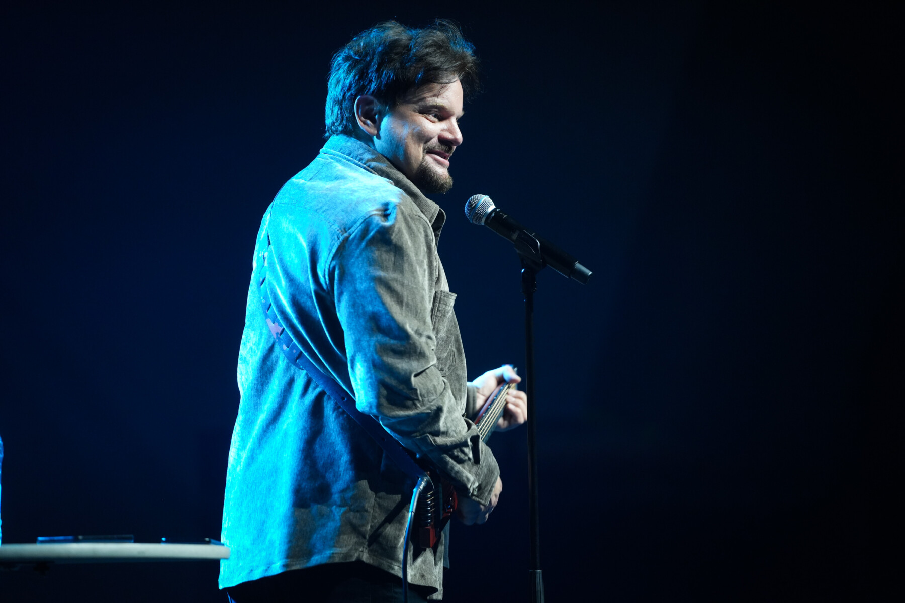 Ismo Leikola performs on stage, lit by blue stage lights, holding a guitar.