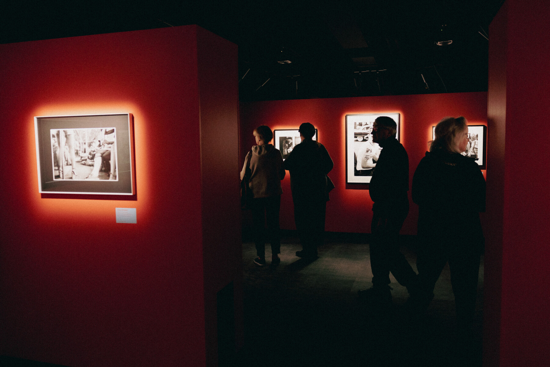 People view illuminated black-and-white photographs displayed on deep red gallery walls at the PLAY photography exhibition in central Oulu.