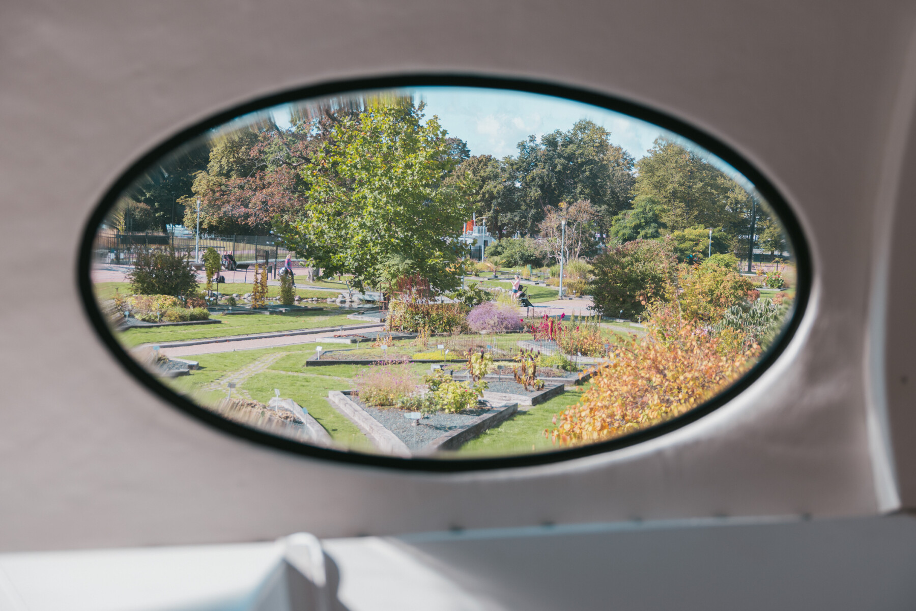 Flower beds and winding paths in a landscaped garden are visible through one of the distinctive oval windows of a Futuro house.