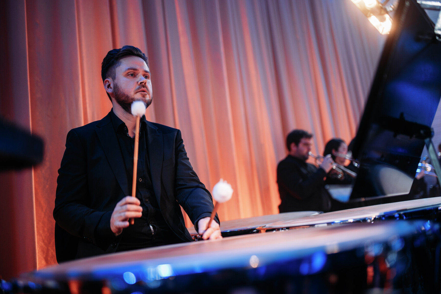 Percussionists in an orchestra, with timpani in the foreground.