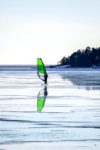 Uma pessoa em uma prancha com uma vela de windsurf se move sobre uma superfície congelada do mar.