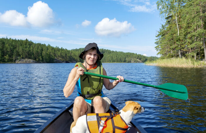 Человек с веслом и собака плывут на каноэ по озеру.